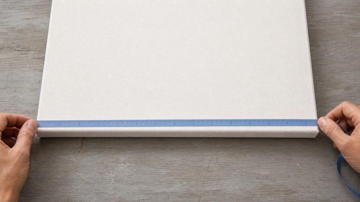 Hands measuring the front outer width of a stretched canvas